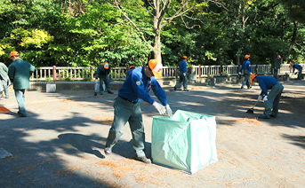 揃いのキャップで公園遊歩道を清掃する所員